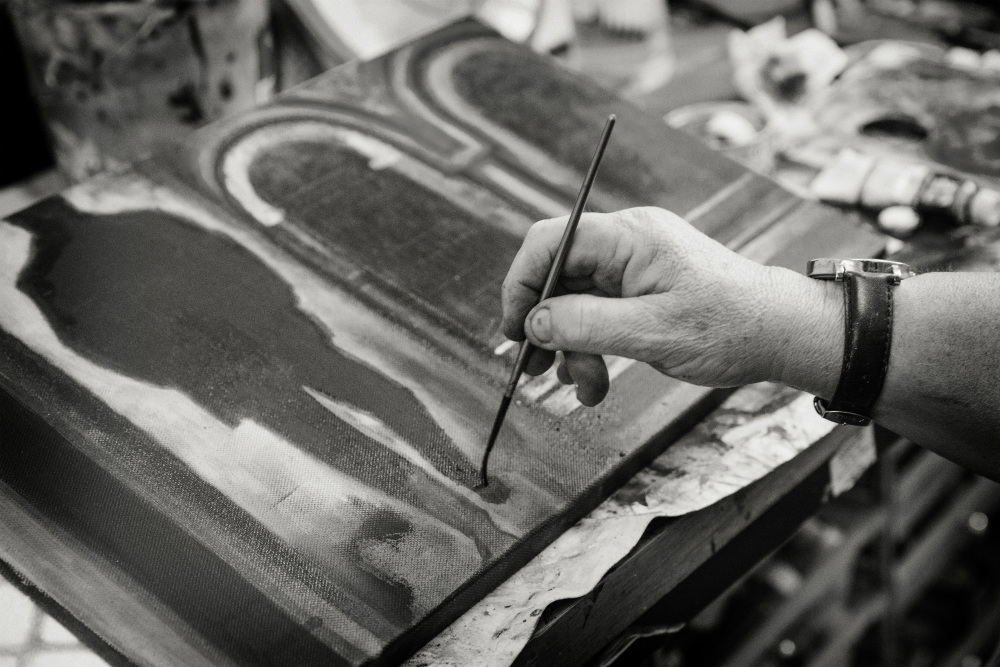 Black and white photo of a hand painting on a canvas.