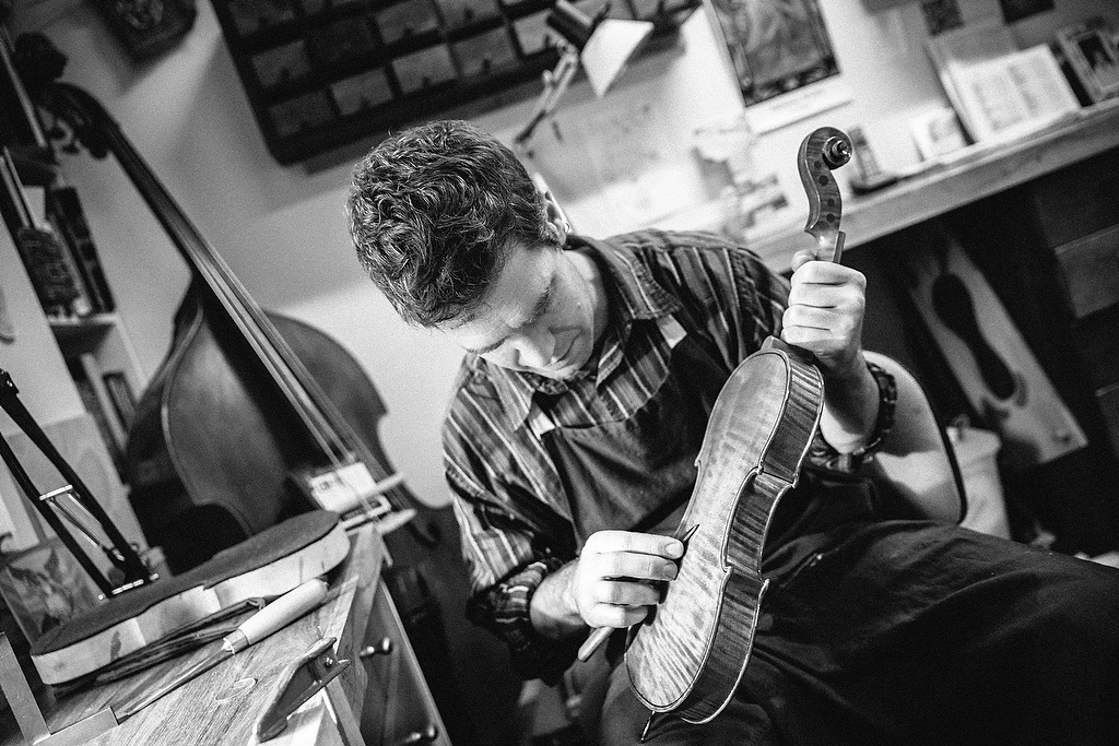 A man wearing an apron and a striped shirt holding a violin.