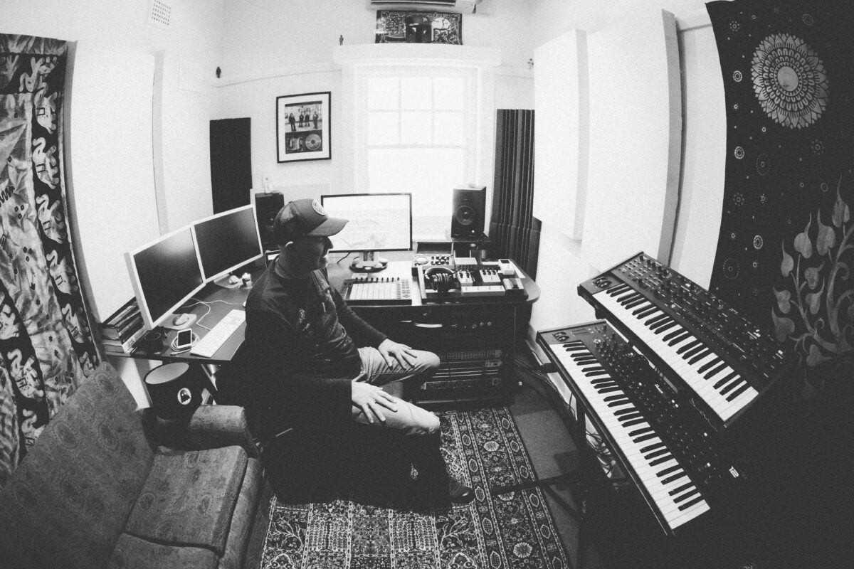 Black and white photo of a man sitting in a room surrounded by electronic music equipment.