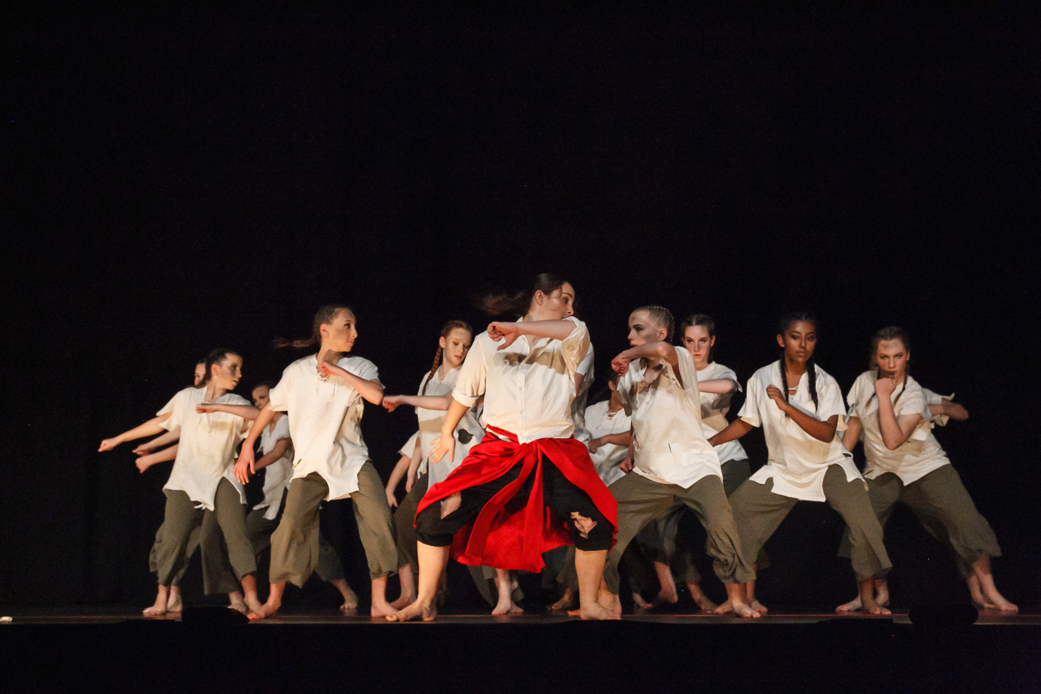 Group of women dancing on stage with a black background, wearing torn white shirts.
