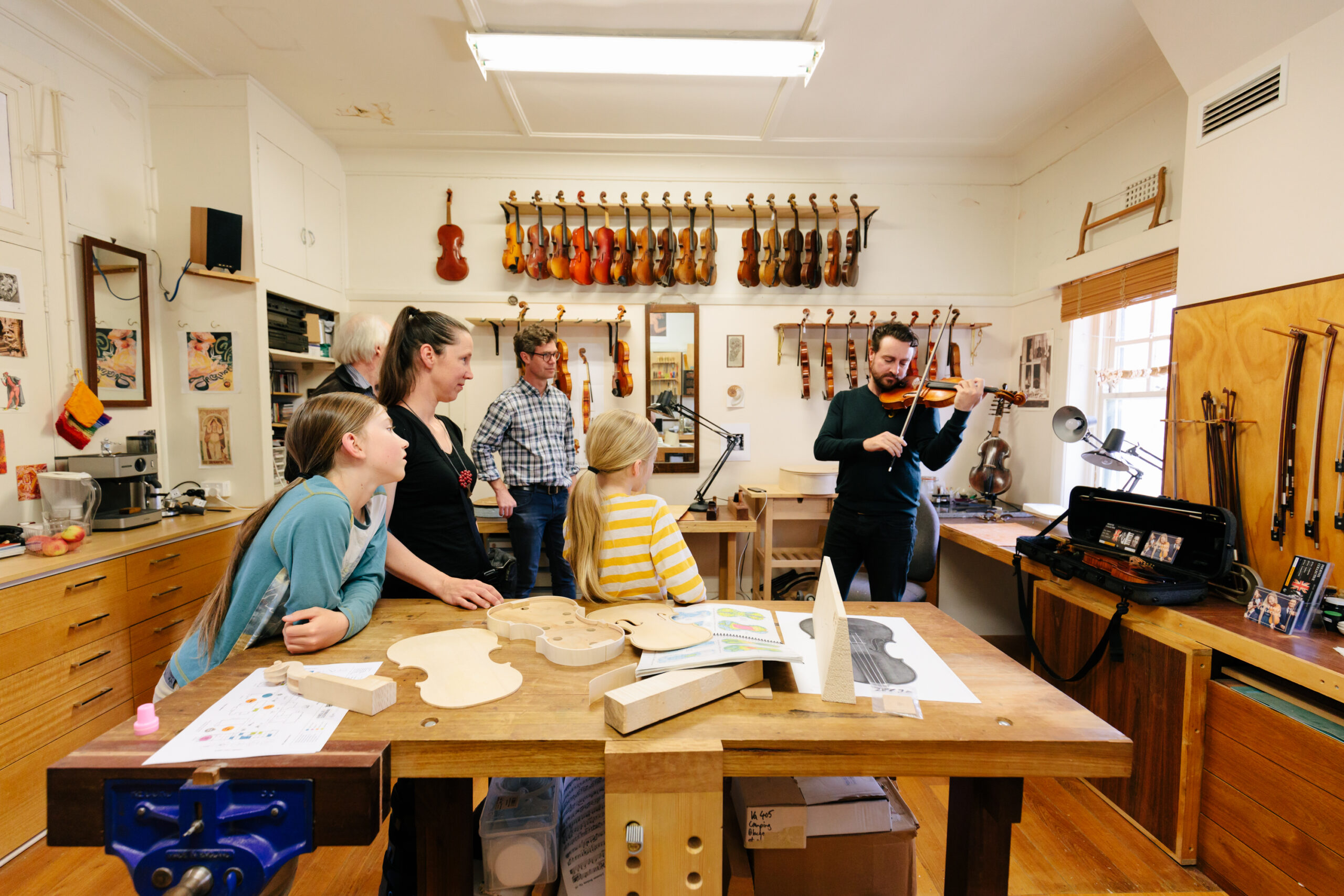 A man playing a violin with 4 people watching on mesmerised