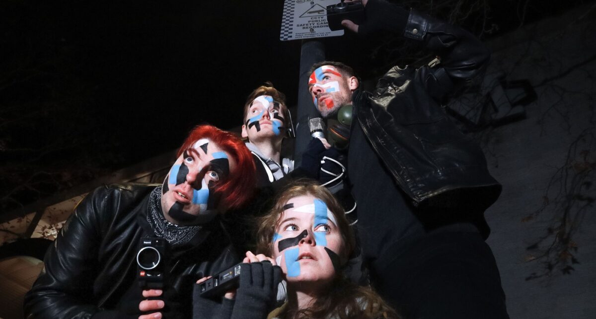 Four people wearing black with coloured face paint.