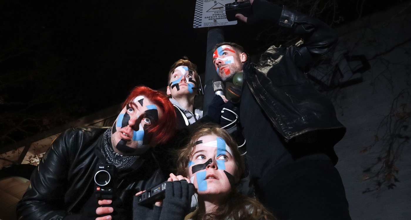 Four people wearing black with coloured face paint.