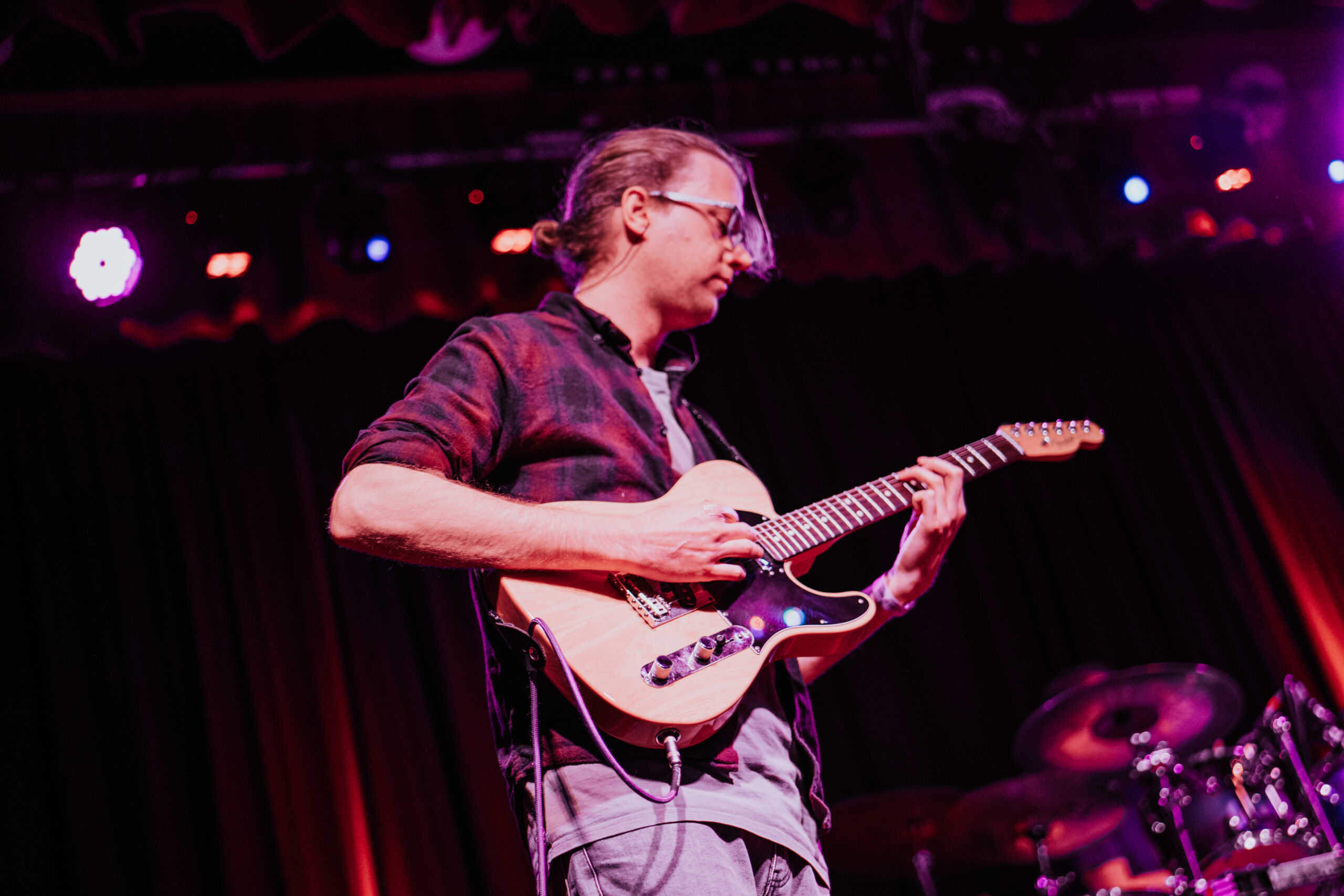 Tom plays guitar on stage wearing a checkered flannelette shirt