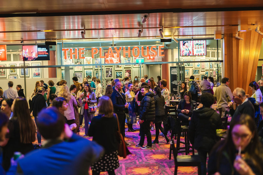 A crowd of people mill around in a neon lit bar.