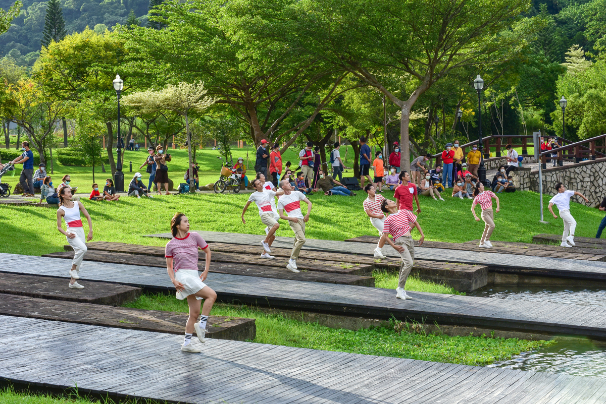 Standing on platforms that hover above bright green grass, the Ku Dancers life one knee in the air and turn their heads upwards.