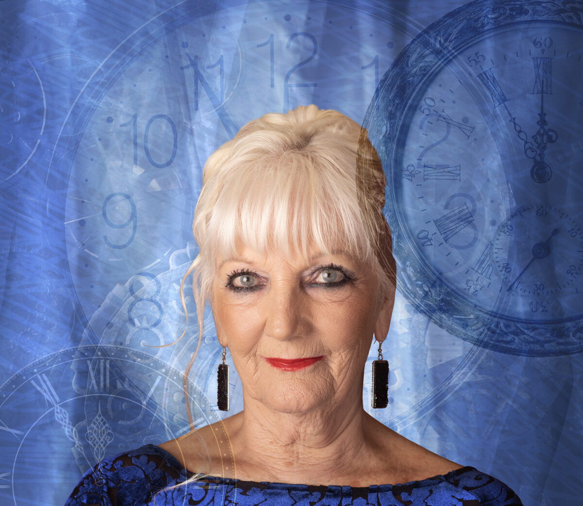 Moya looks directly at the camera wearing red lipstick with blue earrings and top.