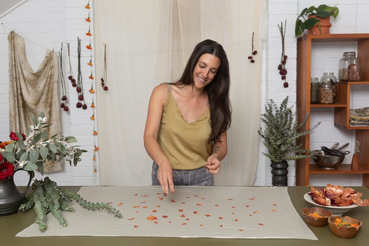Katie with brown hair and light top spinkles flower petals onto a sheet of fabric